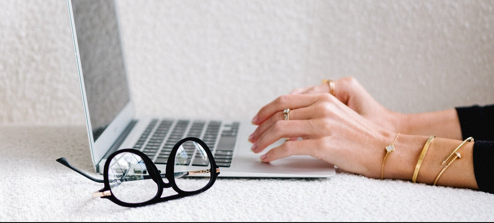 Person using a laptop on a white couch with blue light blocking glasses next to the computer