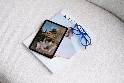 Blue velvet Mykonos Aviator blue light glasses resting on top of a Kinfolk magazine beside an iPad, placed on a soft boucle couch in neutral, cozy tones. The scene feels calm and modern, emphasizing the stylish velvet texture and relaxed workspace vibe.