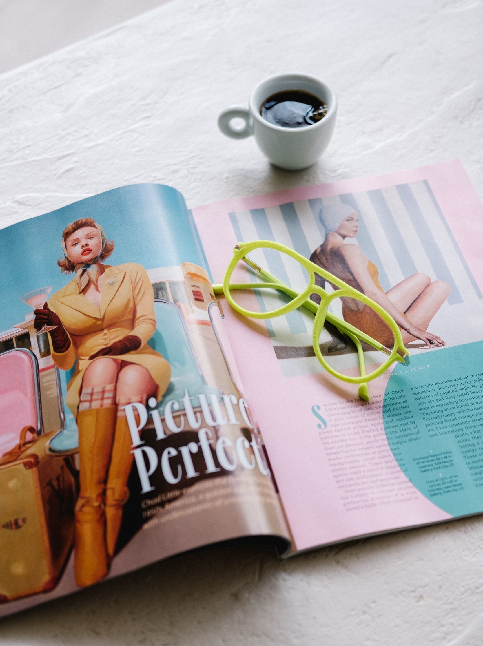 Neon green velvet aviator glasses resting on an open Art Deco–inspired pastel magazine with a cup of espresso beside it on a white table. The image highlights the bold, vibrant frames in a chic, lifestyle setting.