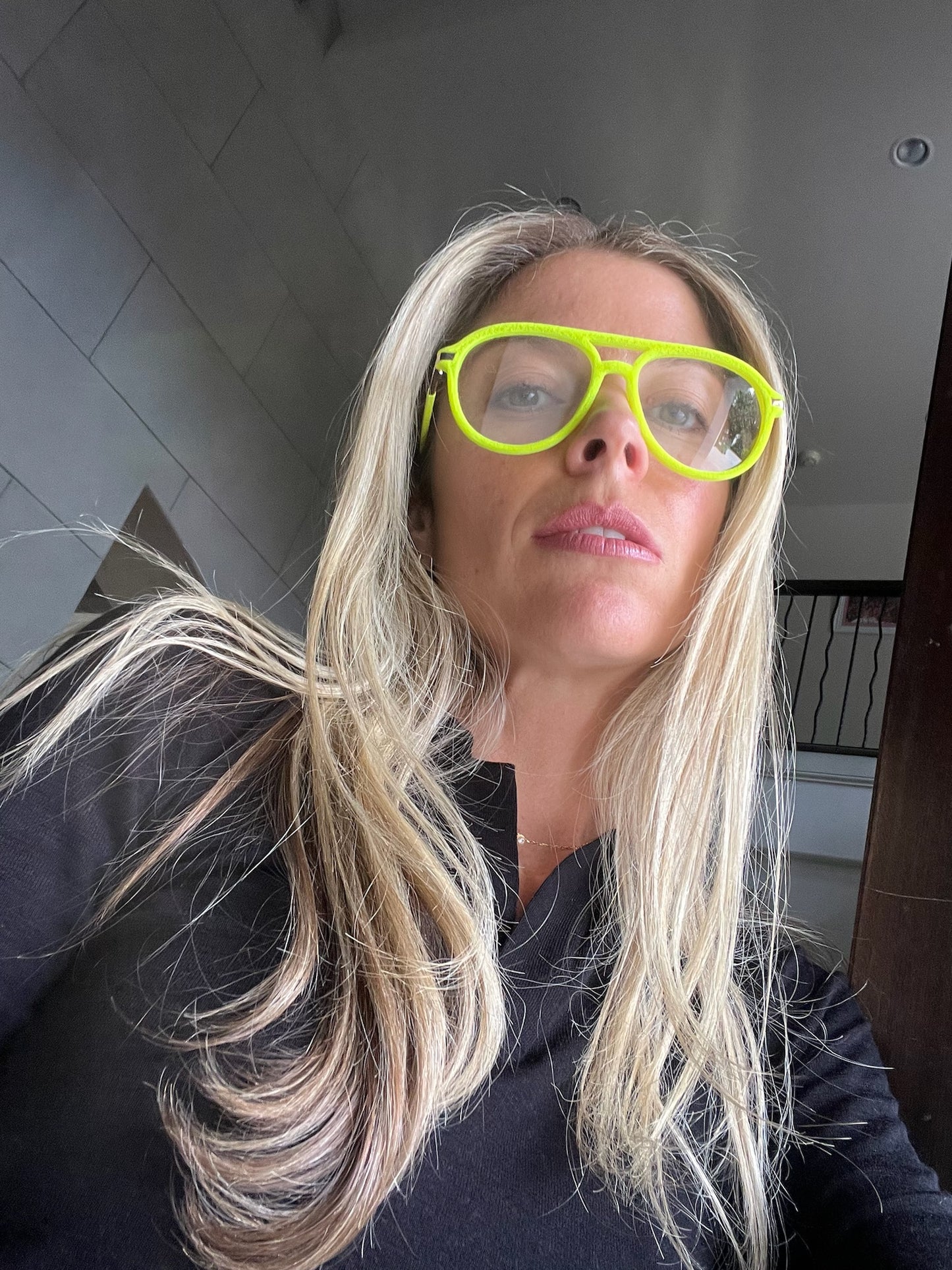 Selfie of a person wearing neon green velvet aviator glasses with blonde hair down and a black top. The bright frames stand out against the simple, chic look.