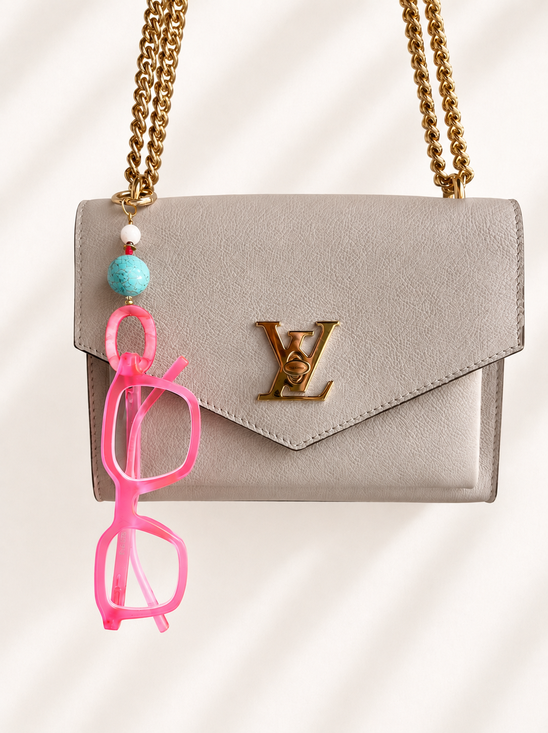 Luxury eyeglass bag charm keychain with a pair of pink blue light glasses hanging on it on a Louis Vuitton purse