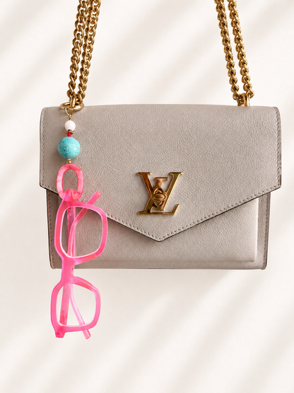 Luxury eyeglass bag charm keychain with a pair of pink blue light glasses hanging on it on a Louis Vuitton purse