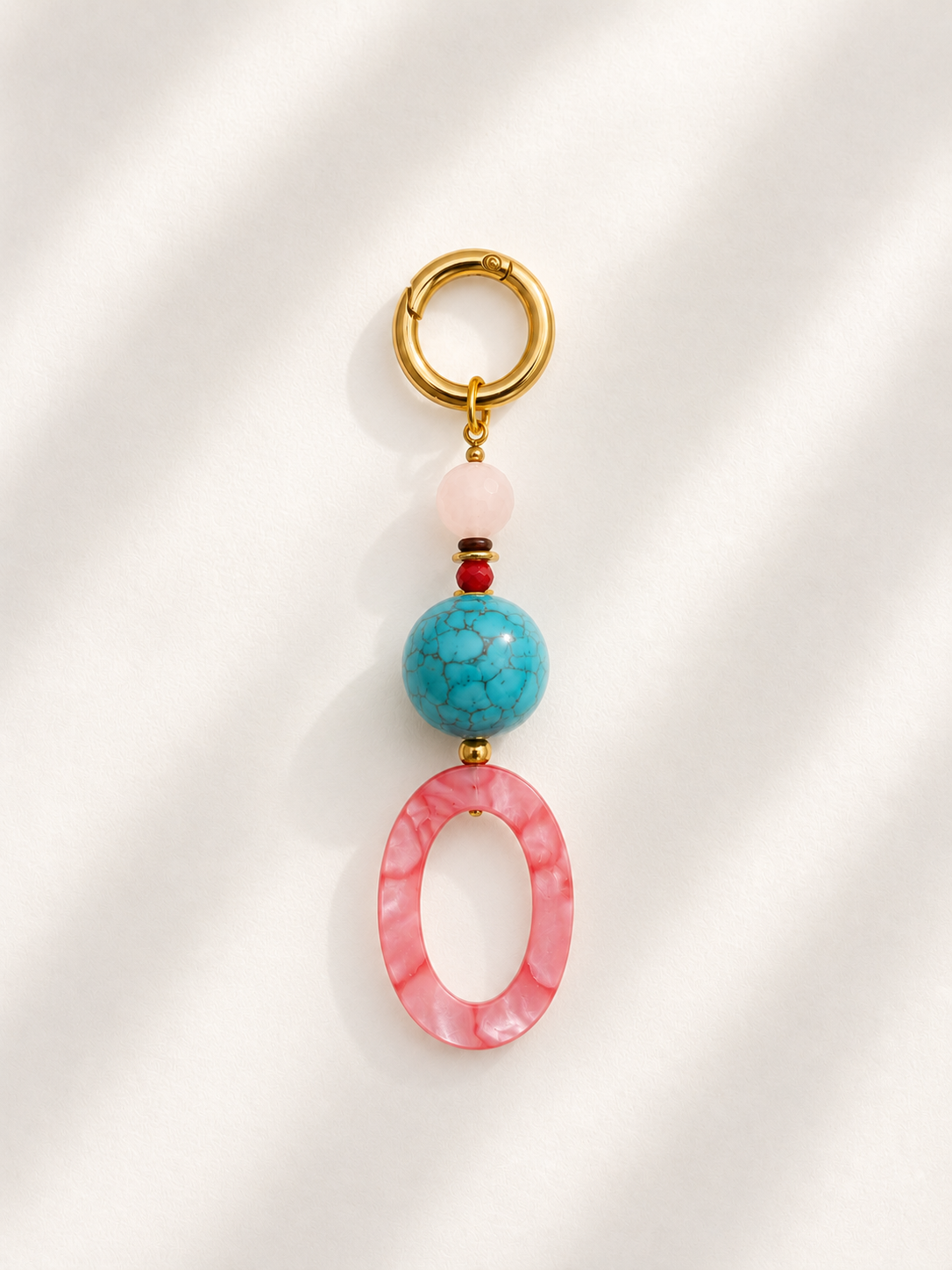 A gold-tone key ring bag charm featuring a pink marbled oval bead, a turquoise blue marbled bead, a light pink round bead, and a tiny red accent bead, displayed on a white background with soft diagonal shadows.