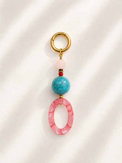 A gold-tone key ring bag charm featuring a pink marbled oval bead, a turquoise blue marbled bead, a light pink round bead, and a tiny red accent bead, displayed on a white background with soft diagonal shadows.